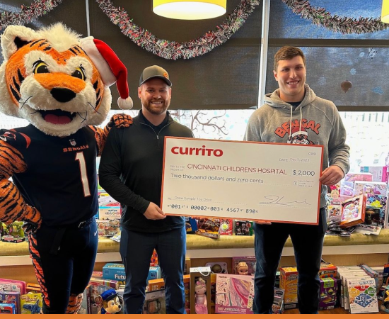 Two men hold a check from Currito to Cincinnati Children's Hospital while the Bengal's tiger mascot stands nearby.